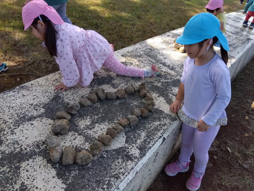 天候にも恵まれ、お散歩日和でした。<br />
今日は昭和記念公園へ散歩に行きました。公園ではドングリやコオロギといった秋の自然や虫探しに夢中で、集めたり、見つけたものを友だちと見せ合ったりとそれぞれに遊びを見つけて自然との触れ合いを楽しんでいました。<br />
石を積んで焼き肉屋さんごっこをしたり、石を使って友だちと電話をごっこを楽しむ子どもたち。石1つで様々なものをイメージさせながら友だちとストーリーを展開させていました。子どもの想像力の豊かさは無限大です！<br />
探索や自由遊びを十分に楽しんだ後はみんなでだるまさんがころんだをしました。一人ひとり態勢が崩れないようにポーズを取りながら少しずつ前へ…<br />
振り返るたびに個性豊かなポーズが見られ可愛らしかったです。